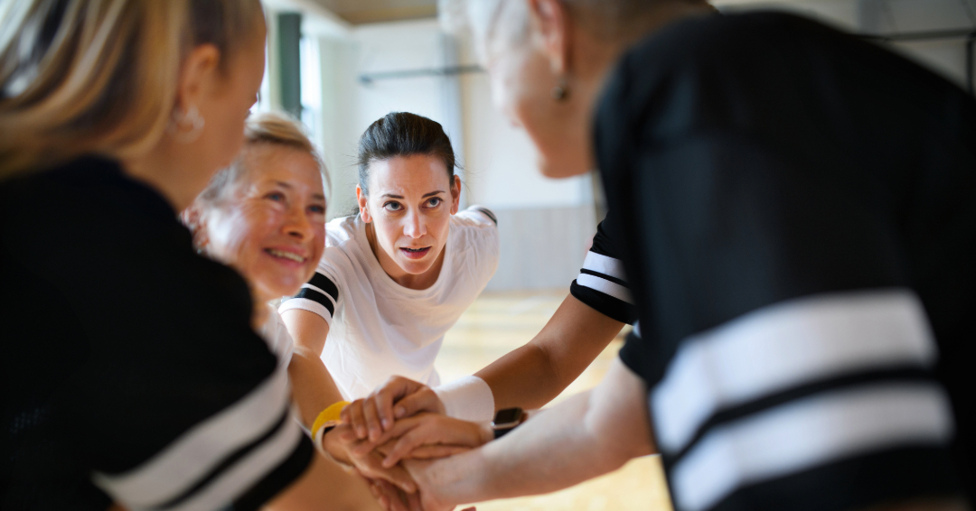 Women of multiple ages gathered in a sports huddle.