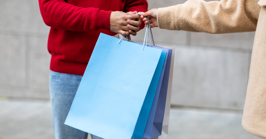 A person hands another person three blue shopping bags.