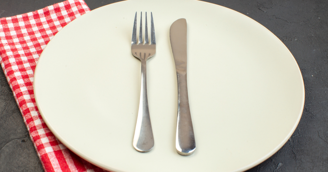 A fork and knife on a white plate, with a red and white gingham napkin tucked underneath. 