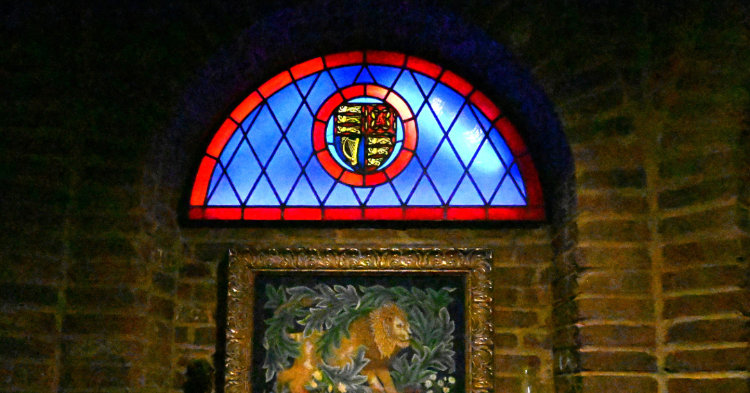 An image of the interior of Castle Gwynn in Arrington, Tennessee, showing a blue and red stained glass window and Medieval artwork of a lion.