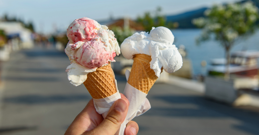2 ice cream cones from an ice-cream shop in downtown Franklin, Tennessee, held by an unseen person's hand; one is vanilla and the other is berry flavored. 