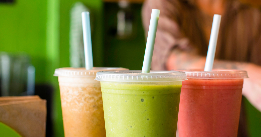 Three organic smoothies, one yellow, one green, and one pink, sit on a counter. 
