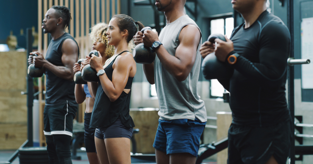 A group of people is working out in a gym, with weights in hand.