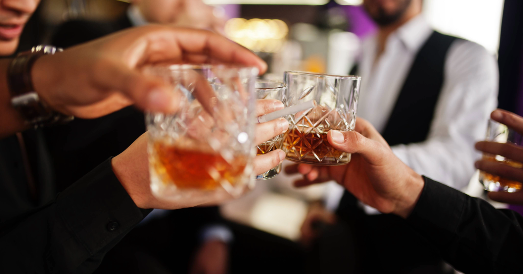A group of friends drinking Tennessee whiskey hold their glasses up to cheers.