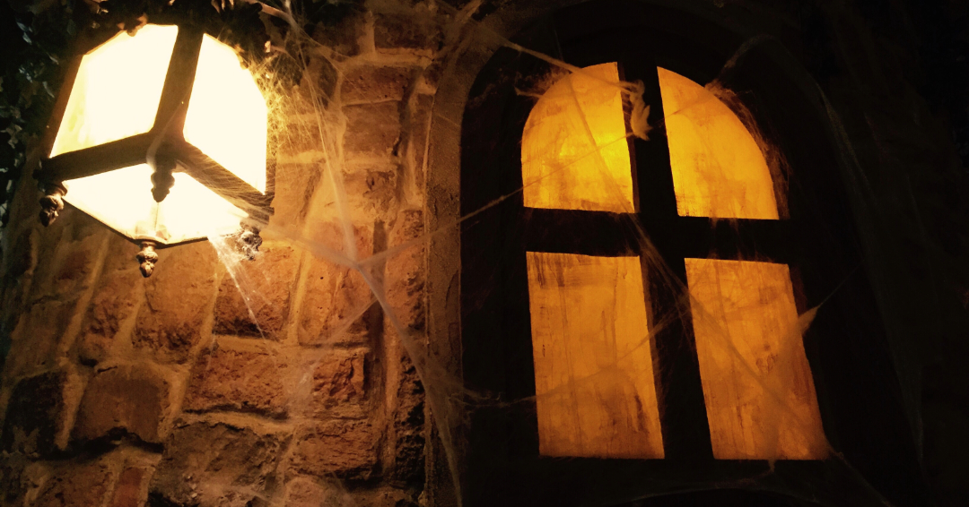 A brick wall with cobwebs, an old-fashioned lantern, and a glowing arched window creates an eerie, haunted atmosphere—perfect for a Franklin Ghost Tour setting.